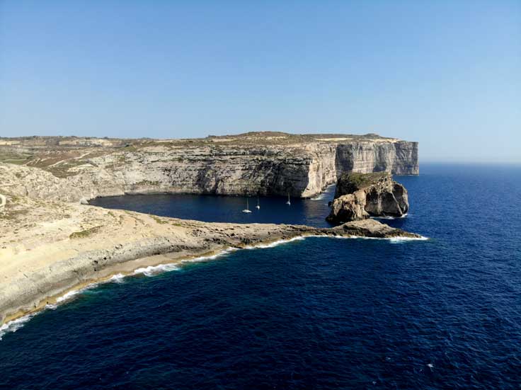 Coastline along Gozo island in Malta, curving limestone cliffs to the left and deep blue coloured ocean to the right